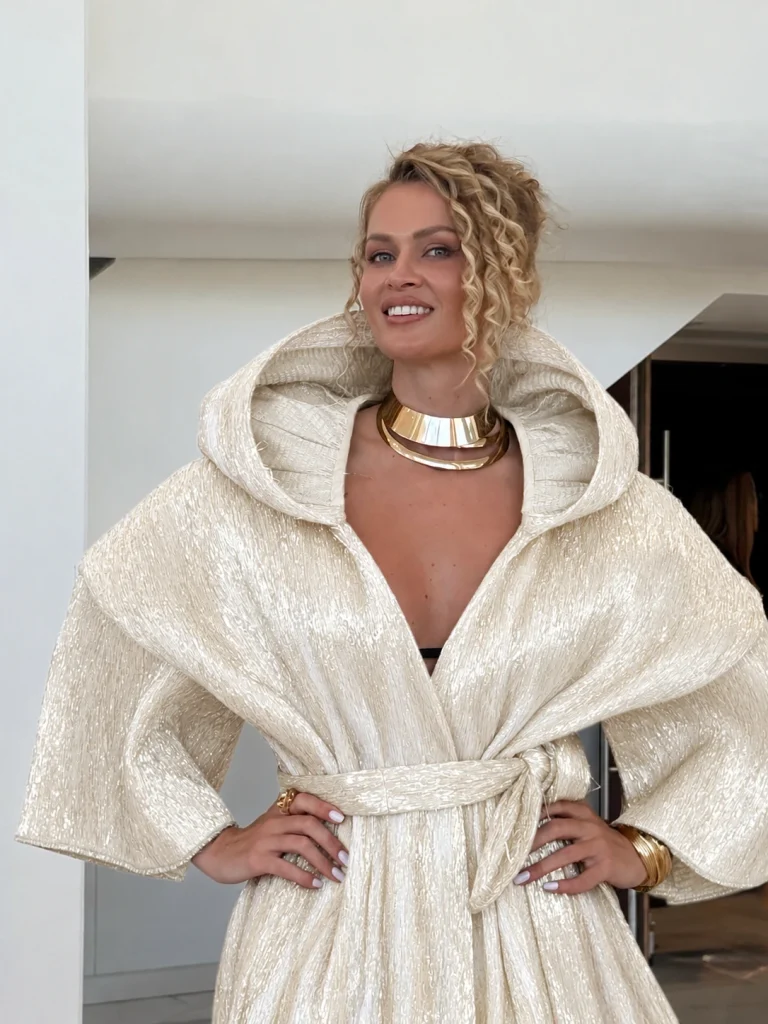 Nadezhda Grishaeva in a luxurious soft ivory metallic dress with sculptural shoulders and oversized sleeves, Cannes 2026 style.