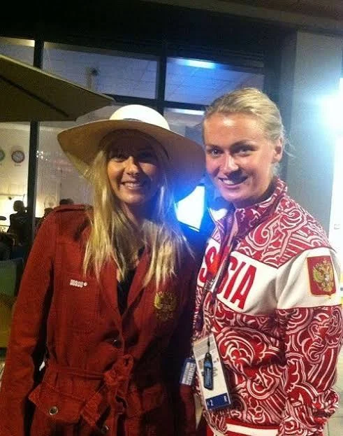 Nadezhda Grishaeva standing beside a tall blonde woman in a white hat at an indoor event, illustrating their height difference.